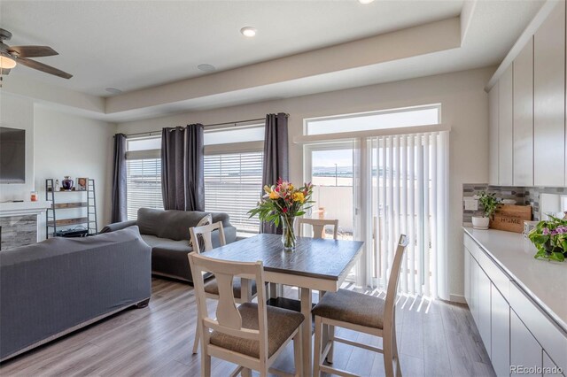 dining space featuring wood-type flooring, ceiling fan, and a raised ceiling