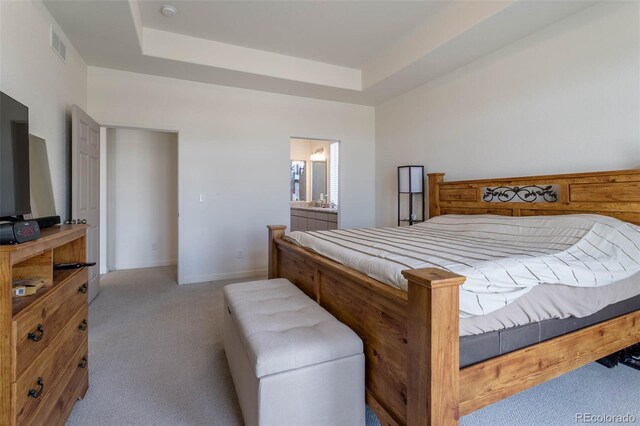 carpeted bedroom with ensuite bath and a raised ceiling