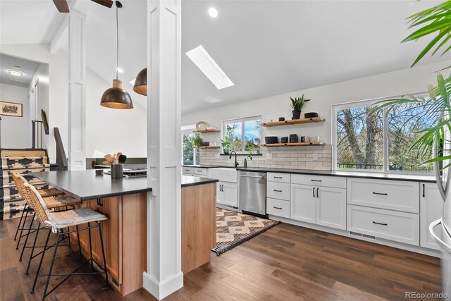 kitchen featuring stainless steel dishwasher, dark countertops, lofted ceiling with skylight, and open shelves
