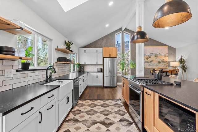 kitchen with stainless steel appliances, dark countertops, vaulted ceiling with skylight, and open shelves