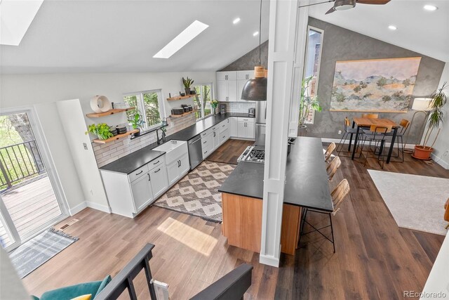 kitchen featuring open shelves, lofted ceiling with skylight, dishwasher, and dark countertops