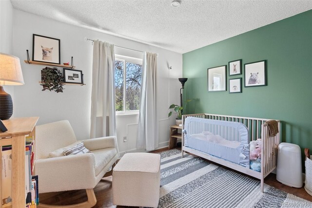 bedroom featuring a crib, a textured ceiling, and wood finished floors