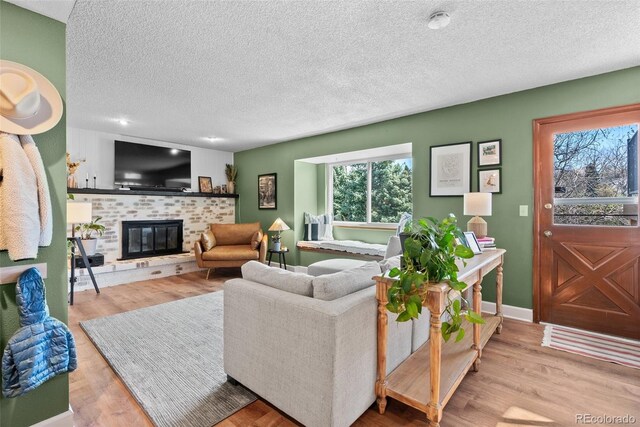 living room with a brick fireplace, a textured ceiling, baseboards, and wood finished floors