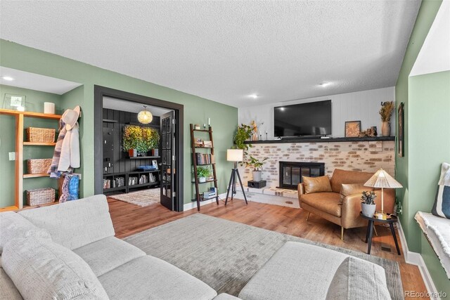 living area featuring baseboards, a textured ceiling, wood finished floors, and a fireplace