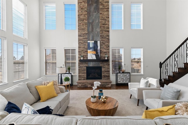 living area with a stone fireplace, stairway, wood finished floors, and a healthy amount of sunlight