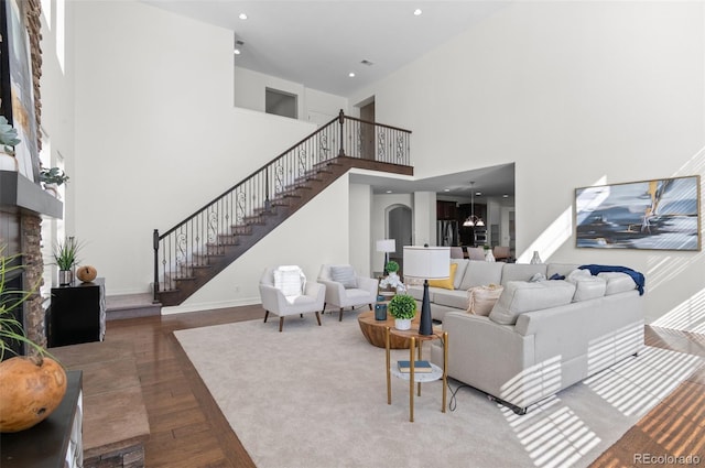 living room featuring a stone fireplace, recessed lighting, a high ceiling, wood finished floors, and stairway