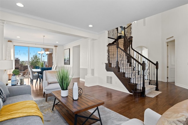 living area featuring visible vents, stairway, wood finished floors, and decorative columns