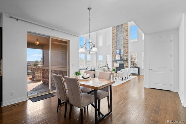 dining room with a notable chandelier, dark wood-style flooring, a fireplace, visible vents, and baseboards