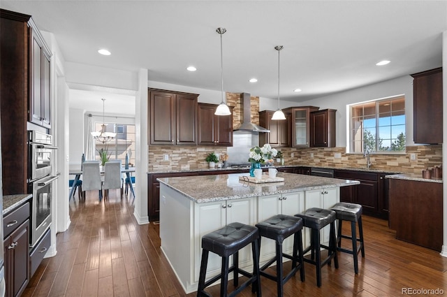 kitchen featuring a center island, dark wood finished floors, wall chimney range hood, and dark brown cabinets