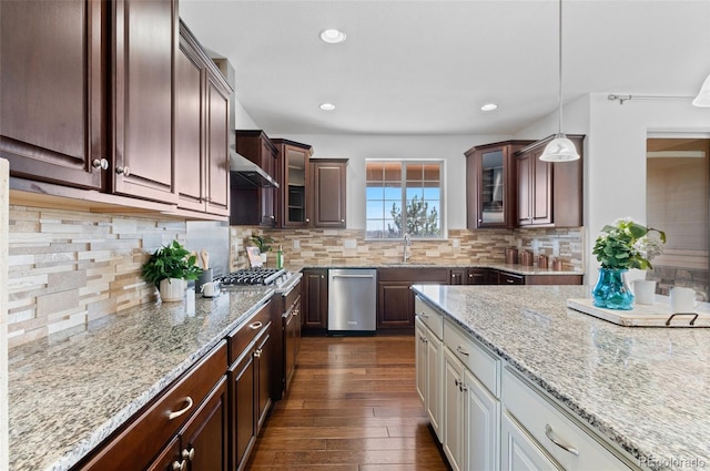 kitchen featuring stainless steel appliances, dark wood-style flooring, wall chimney range hood, glass insert cabinets, and pendant lighting