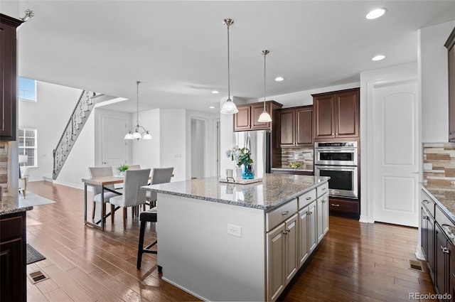 kitchen with appliances with stainless steel finishes, a kitchen island, dark wood finished floors, and tasteful backsplash