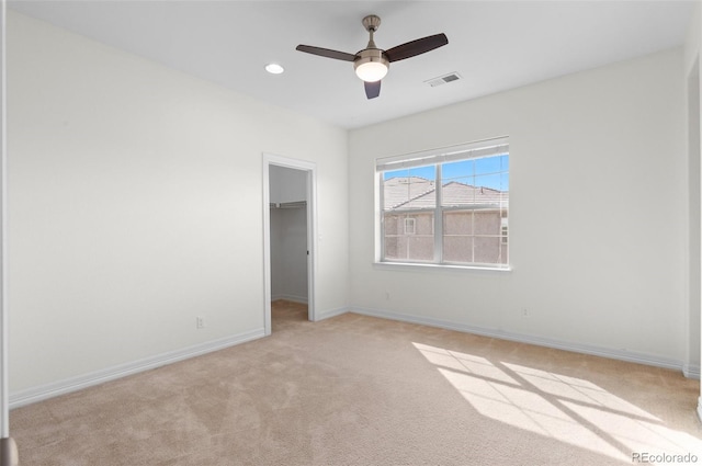 unfurnished bedroom with a walk in closet, light carpet, visible vents, and baseboards