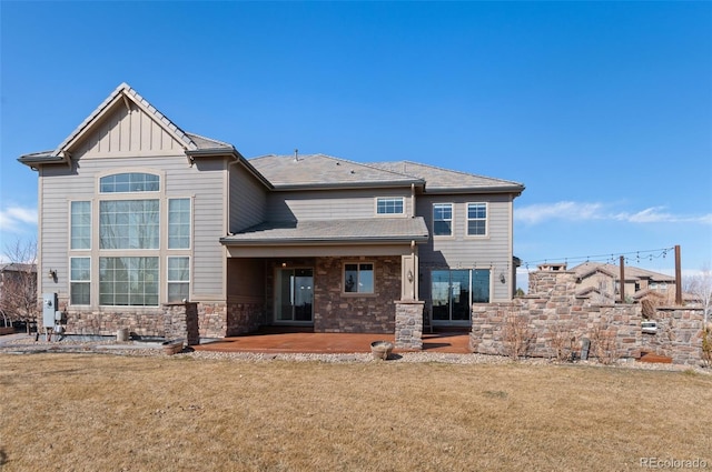 back of property with a patio, a yard, board and batten siding, and stone siding