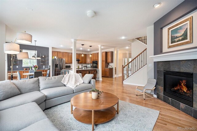 living area featuring stairs, light wood-style floors, a tiled fireplace, recessed lighting, and decorative columns