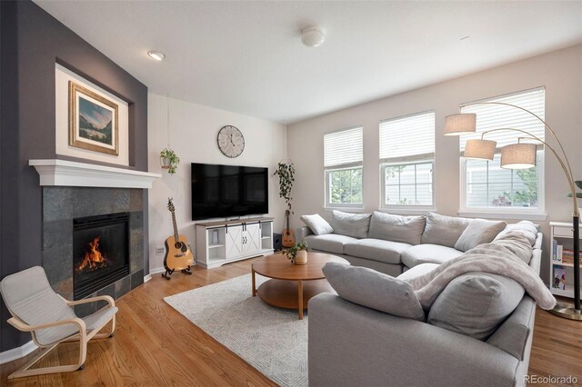 living room with a tiled fireplace, light wood finished floors, and baseboards