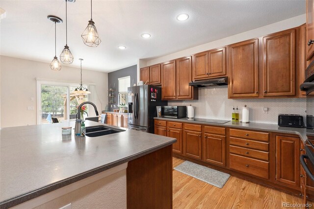 kitchen with stainless steel appliances, under cabinet range hood, light wood-style floors, a sink, and hanging light fixtures
