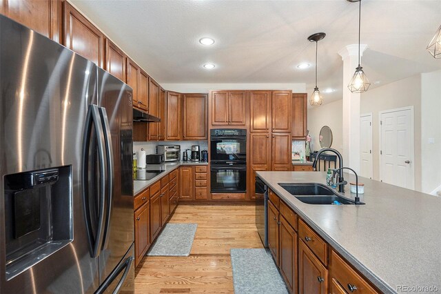 kitchen featuring black appliances, a sink, under cabinet range hood, brown cabinetry, and light wood-style flooring