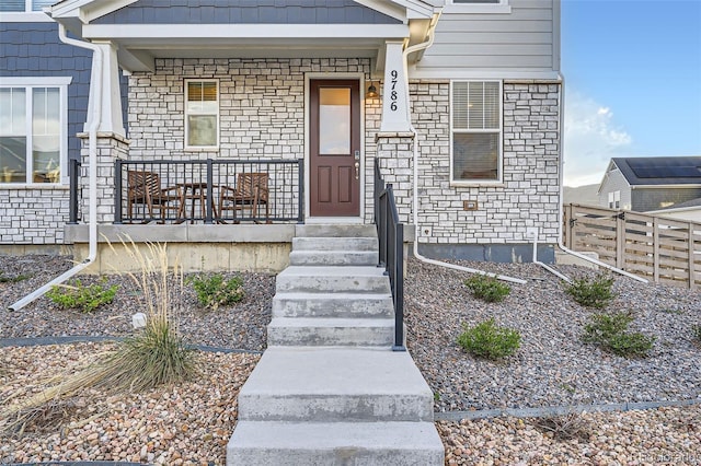entrance to property featuring stone siding, a porch, and fence
