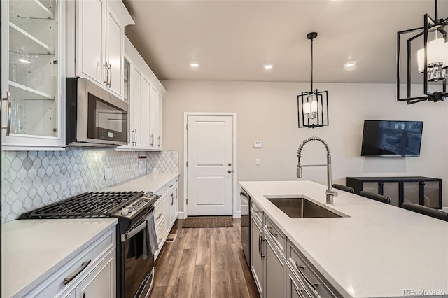 kitchen featuring stainless steel appliances, a sink, dark wood-style floors, decorative backsplash, and glass insert cabinets
