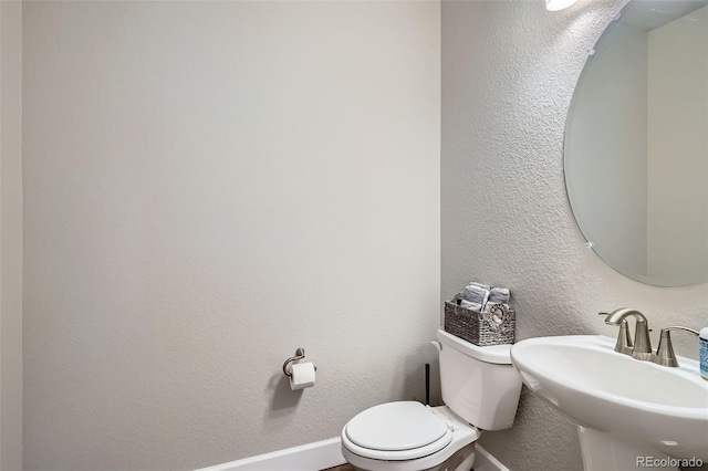 half bath featuring a sink, toilet, baseboards, and a textured wall