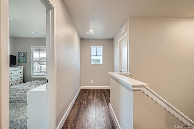 corridor with a textured wall, dark wood-style floors, baseboards, and an upstairs landing