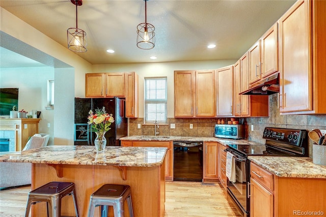 3354 Wabash St, Denver, CO 80238 - kitchen featuring black appliances, under cabinet range hood, light wood-style flooring, a breakfast bar area, and a kitchen island