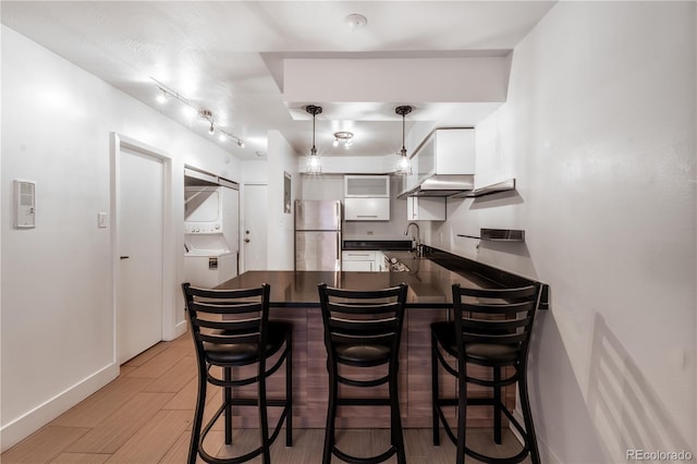 830 N Sherman St Unit 105, Denver, CO 80203 - kitchen with freestanding refrigerator, dark countertops, a peninsula, stacked washer / drying machine, and a breakfast bar