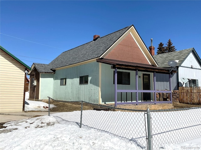 snow covered rear of property featuring a porch, a shingled roof, and fence