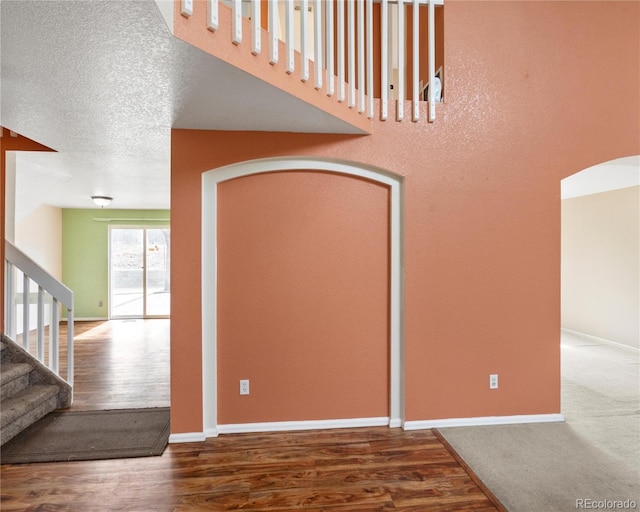 stairway with wood finished floors, arched walkways, baseboards, and a textured ceiling