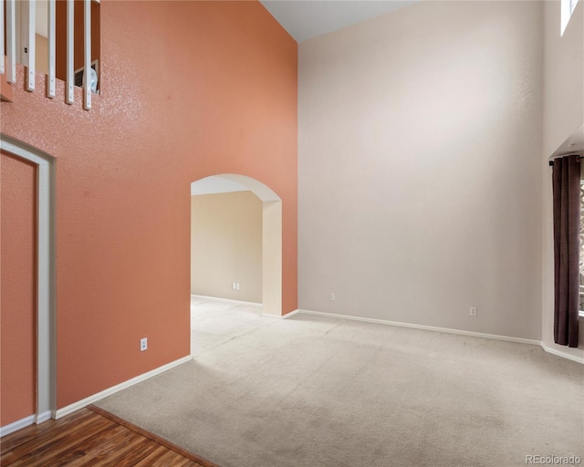 carpeted spare room with baseboards, a high ceiling, and arched walkways