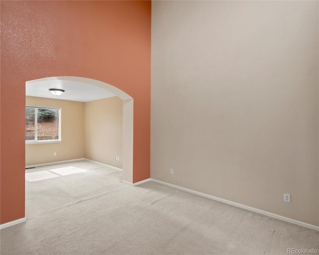 carpeted empty room with baseboards and arched walkways