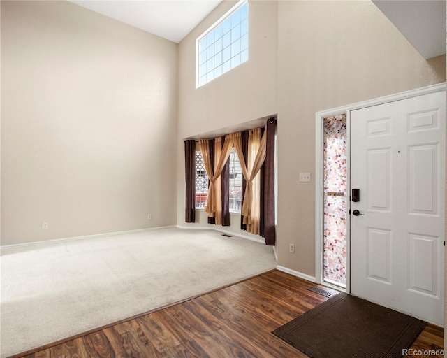 entrance foyer with baseboards, visible vents, a towering ceiling, and wood finished floors