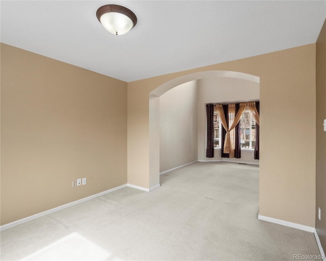 carpeted empty room with baseboards and arched walkways