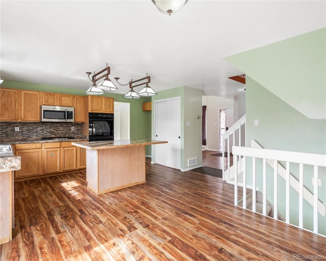 kitchen featuring backsplash, a kitchen island, appliances with stainless steel finishes, visible vents, and dark wood-style flooring