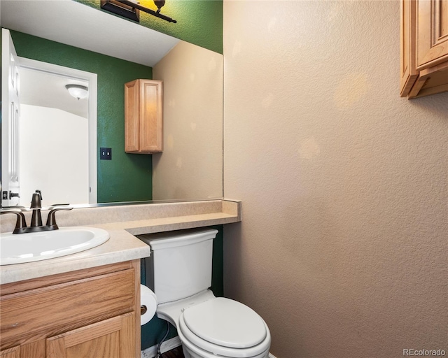 half bathroom featuring a textured wall, toilet, and vanity