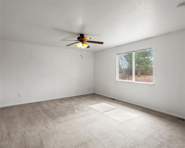 carpeted spare room with a textured ceiling, visible vents, baseboards, and a ceiling fan