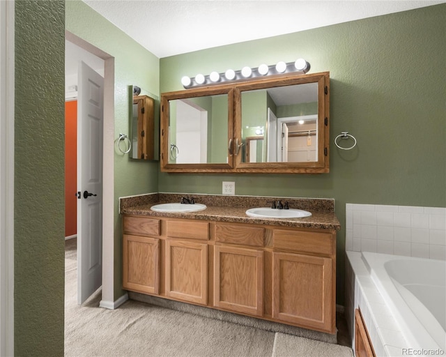 bathroom featuring a tub to relax in, double vanity, a textured wall, and a sink