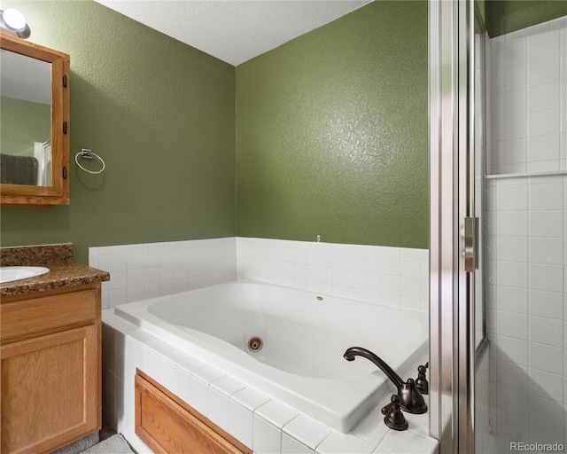 full bathroom with a shower stall, a textured wall, vanity, and a jetted tub