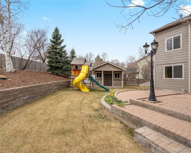 view of jungle gym featuring a lawn, an outbuilding, a fenced backyard, and a patio area