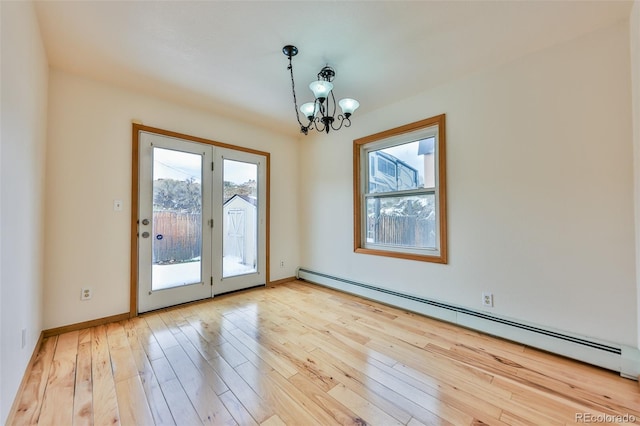 spare room featuring a chandelier, a wealth of natural light, baseboard heating, and light wood-type flooring