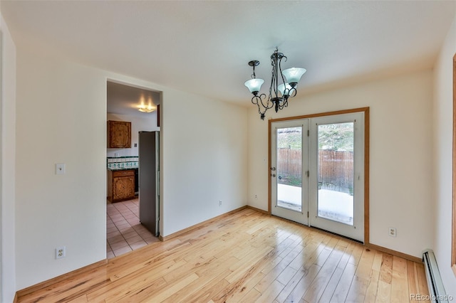 spare room with a baseboard radiator, light wood-type flooring, and an inviting chandelier