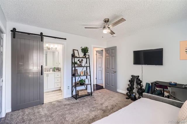 bedroom with carpet, ceiling fan, a barn door, a textured ceiling, and connected bathroom