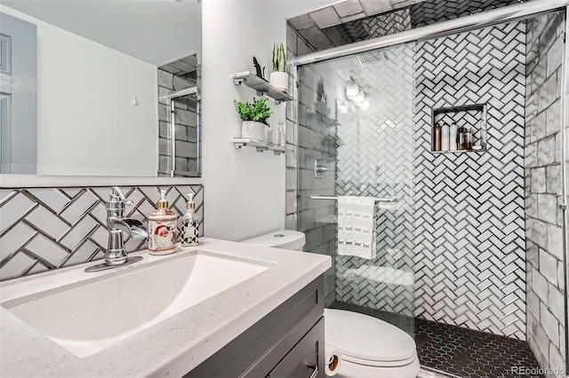 bathroom with vanity, toilet, a shower with door, and backsplash