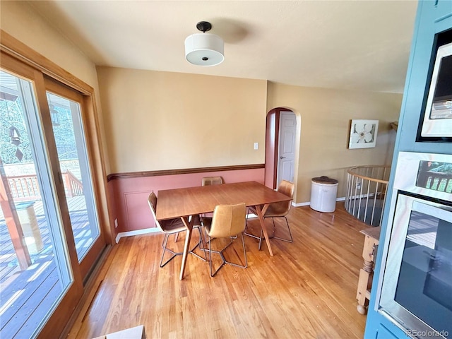 dining area with arched walkways and light wood-type flooring