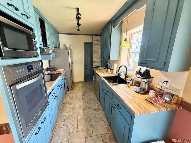 kitchen with appliances with stainless steel finishes, blue cabinets, a sink, wood counters, and stone tile flooring