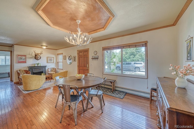dining room featuring an inviting chandelier, ornamental molding, hardwood / wood-style flooring, a fireplace, and baseboard heating