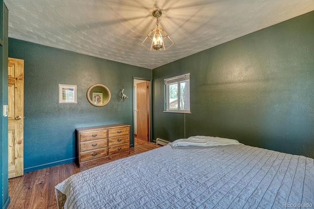 bedroom with baseboards, wood finished floors, a baseboard heating unit, and a textured wall