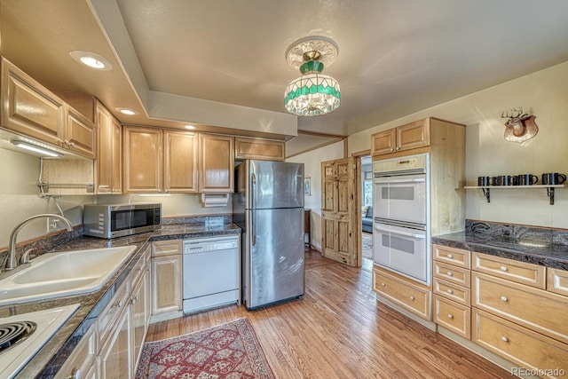 kitchen with a sink, dark countertops, appliances with stainless steel finishes, light brown cabinetry, and light wood-style floors