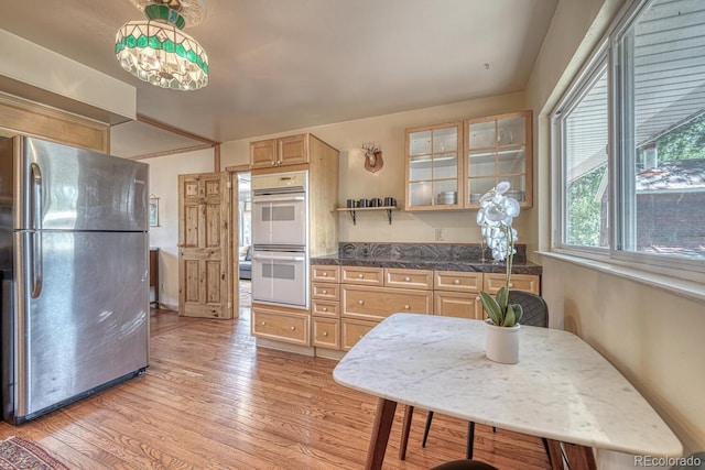 kitchen featuring glass insert cabinets, light brown cabinets, light wood-type flooring, freestanding refrigerator, and double oven