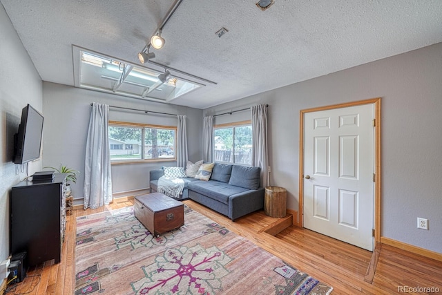living area with a textured ceiling, wood finished floors, baseboards, and a healthy amount of sunlight